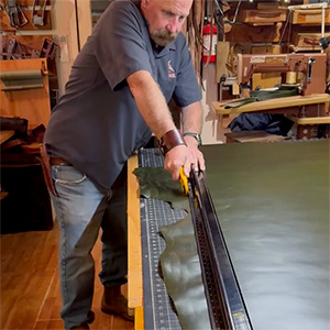 Leathersmith cutting a large green cowhide with a hand