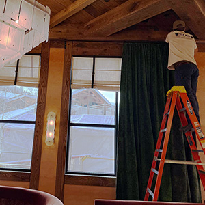 Person on a ladder installing the window treatment over a tall window