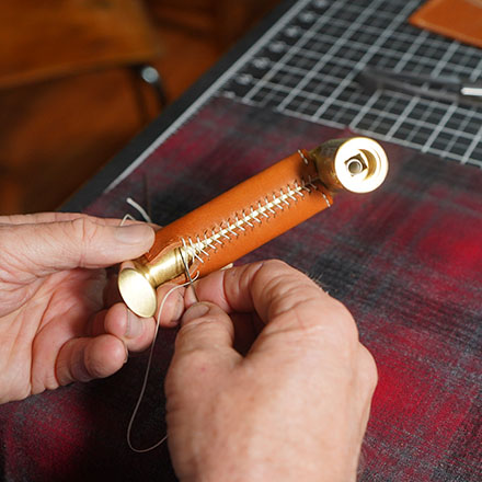 A person hand stitching leather wrap over a brass door handle
