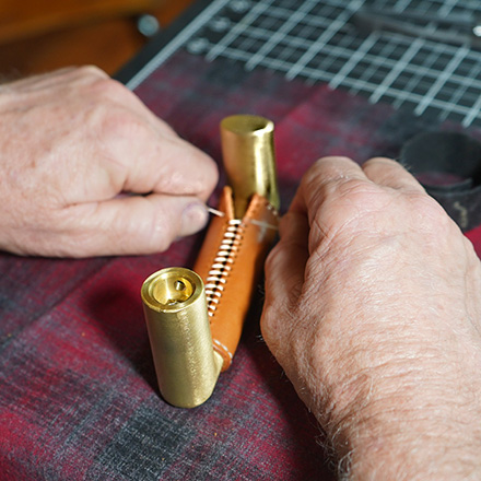 A person pulling on the threads of the leather wrap over a brass door handle