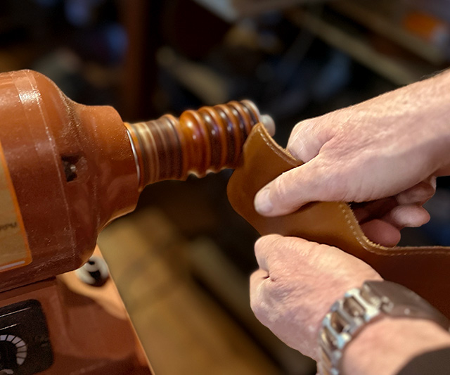 Leathersmith burnishes the edge of a leather wallet with burnisher machine