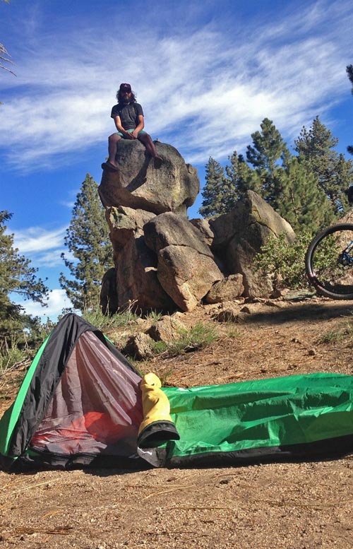 Jay sitting on top of tall rocks with his tent in the foreground.