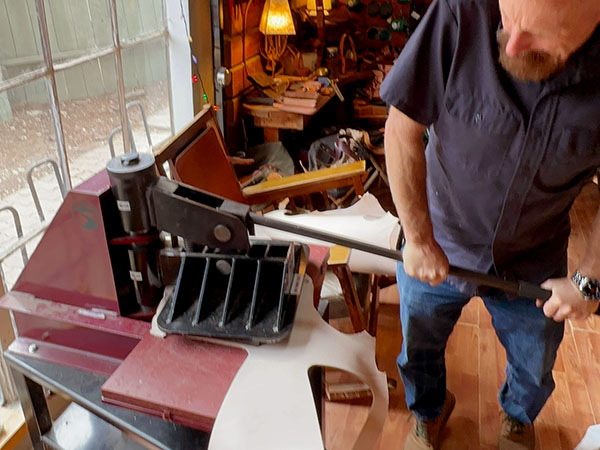 Worker pushes down the press arm to cut out a piece of leather