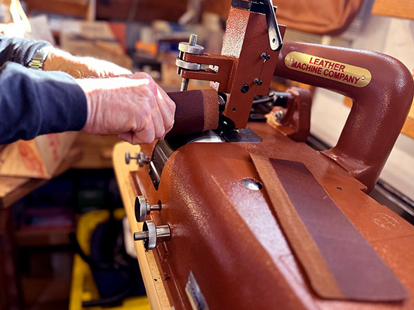 Worker feeds a piece of leather through the skiver machine