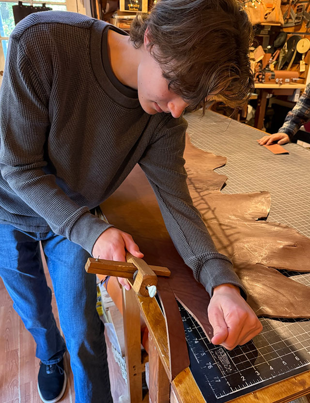 Guy cutting a leather strap out of a hide over a table