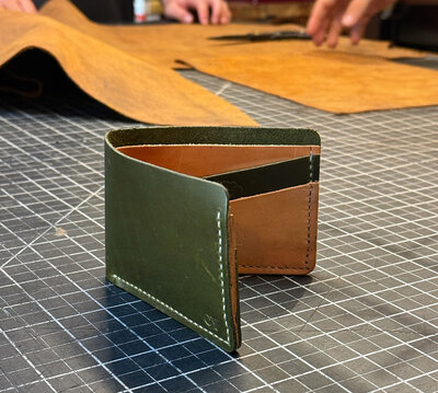 A custom bi-fold wallet with green leather on the outside and alternating tan/green leather for the inside pockets